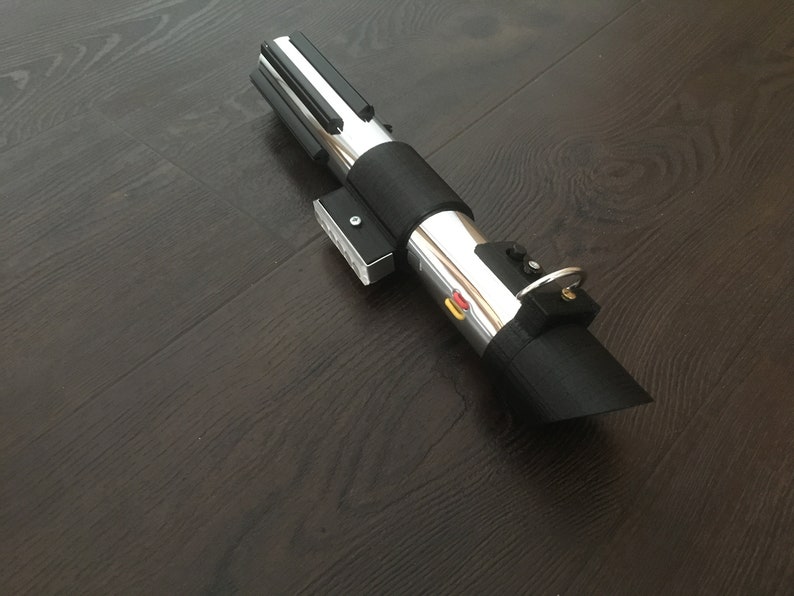 Pu&ograve; includere: Un accessorio per spada laser nero e argento con un'impugnatura nera e una lama argentata. L'impugnatura ha un pulsante nero e un anello argentato.