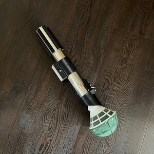 Pu&ograve; includere: Una spada laser nera e argentata con una palla di schiuma floreale verde attaccata all'estremit&agrave;.