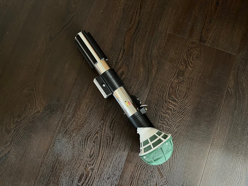 Pu&ograve; includere: Una spada laser nera e argentata con una palla di schiuma floreale verde attaccata all'estremit&agrave;.