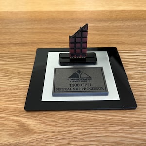 Può includere: Un espositore nero e argento con un modello di chip per computer stampato in 3D. Il chip è etichettato "Cyclone Systems T800 CPU Neural Net Processor".