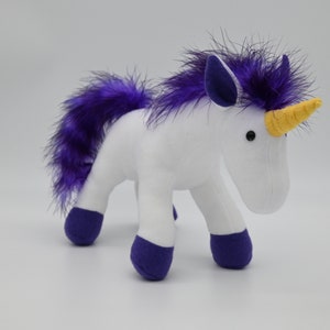 May include: A white plush unicorn with purple accents. The unicorn has a purple mane and tail, purple hooves, and a yellow horn. The toy is standing on all four legs and has black button eyes. A whimsical stuffed animal.