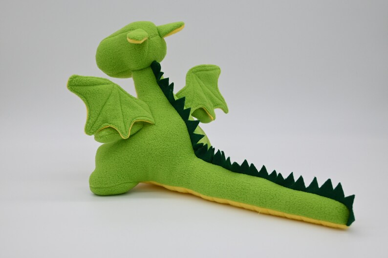 May include: Green plush dragon toy with yellow accents. The dragon has wings, a long tail with green spikes, and a small horn on its head.