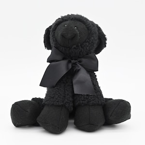 May include: A black plush dog toy with a black satin bow around its neck. The dog has a fluffy, textured body and solid black paws. The toy is sitting upright against a white background.