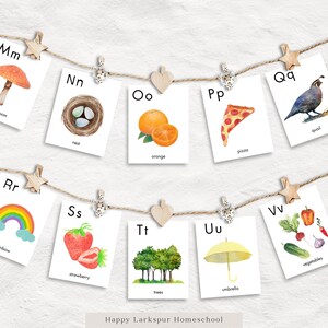 May include: A set of alphabet flashcards with watercolour illustrations. Each card features a letter, a picture, and a word. The letters are Mm, Nn, Oo, Pp, Qq, Rr, Ss, Tt, Uu, and Vv. The pictures include a mushroom, a nest, an orange, a pizza, a quail, a rainbow, a strawberry, trees, an umbrella, and vegetables.