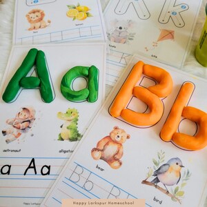 May include: A set of printable alphabet worksheets for kids featuring colorful playdough letters, illustrations of animals, and lines for tracing the letters. The text "Happy Larkspur Homeschool" is at the bottom of the page.