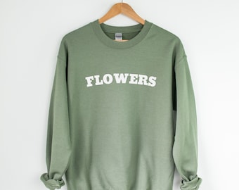 Op de afbeelding: Een saliegroen sweatshirt met het woord "FLOWERS" in wit op de voorkant.