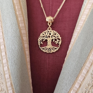 May include: A gold-toned necklace featuring a circular pendant with an intricate tree of life design. The pendant is suspended from a delicate gold-toned chain, showcasing detailed branches and roots within a circular frame, creating a cohesive piece.