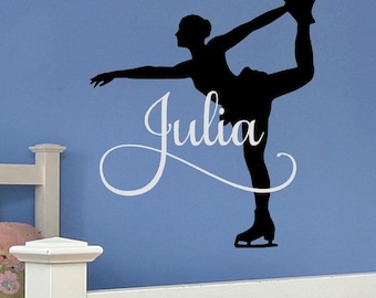 May include: A black wall decal silhouette of a figure skater in a pose with one leg extended upward, featuring the name Julia written in white cursive script across the center of the skater's body on a blue wall surface.