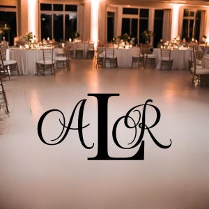 May include: A large black vinyl monogram decal featuring the letters A, L, and R in a decorative script font, applied to a smooth white floor in a banquet hall setting with round tables and chairs visible in the background.