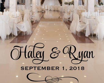 May include: A black vinyl floor decal applied to a glossy white tile surface in a banquet hall. The decal features the names Haley & Ryan in a script font, the date SEPTEMBER 1, 2018 in a sans-serif font, and a decorative flourish below.