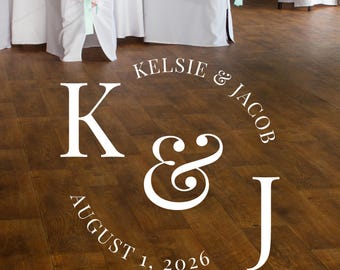May include: White lettering on a dark wood floor announces a wedding. The text includes the names Kelsie & Jacob, the date August 1, 2026, and the initials K & J. Wedding decor.