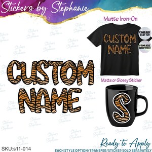 May include: A custom name graphic with a tiger stripe pattern in orange and black. The image displays the text on a black t-shirt and a black mug, with labels for matte iron-on, printable glitter, printable iridescent, and matte or glossy sticker.