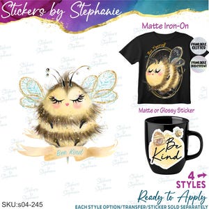 May include: A graphic design featuring a fluffy bee with closed eyes and long lashes, sitting on a banner that reads Bee Kind. A black t-shirt displays the bee inside a gold oval with the text Bee Yourself, and a black mug shows a bee and hive.
