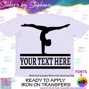 May include: A light-colored t-shirt featuring a black silhouette of a gymnast performing a handstand on a balance beam. Below the gymnast, the text "YOUR TEXT HERE" is printed in bold black capital letters between two horizontal black lines.
