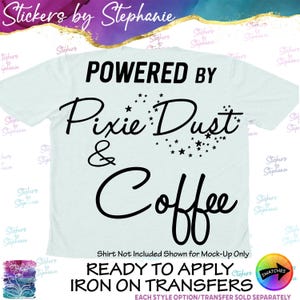 May include: A light blue t-shirt featuring black text that reads POWERED BY Pixie Dust & Coffee, with the word Pixie Dust surrounded by small star graphics. The design is a ready-to-apply iron-on transfer for apparel customization.