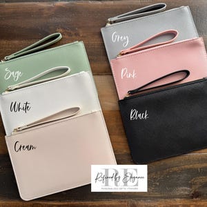 May include: A collection of six rectangular clutch bags in various colors: sage, white, cream, grey, pink, and black. Each bag has a matching wrist strap and a zipper closure. The names of the colors are written on each bag.