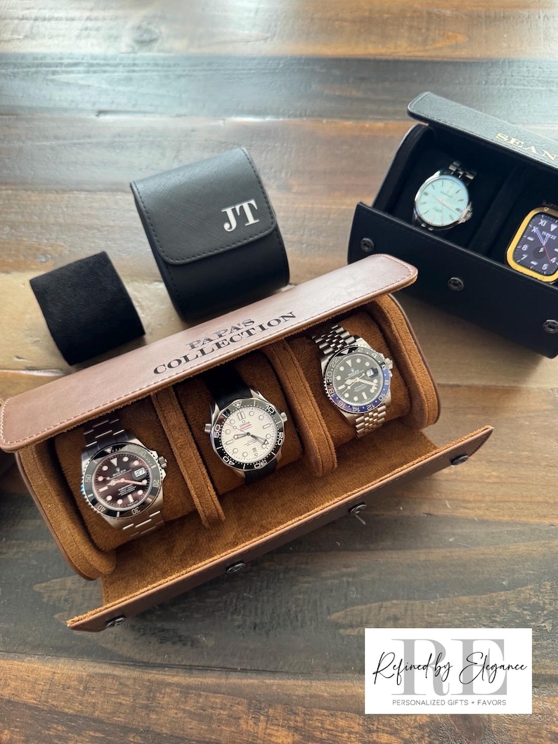 May include: A brown leather watch roll with three slots for watches. The watch roll has the text "Papa's Collection" embossed on the front. There are three watches in the slots, one with a black face, one with a white face, and one with a blue face. The watch roll is on a wooden surface.