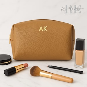 May include: A tan leather cosmetic bag with gold zipper and the initials "AK". Makeup items include a lipstick, makeup brush, foundation, eyeliner, and a compact. The bag is labeled "Refined by Elegance".