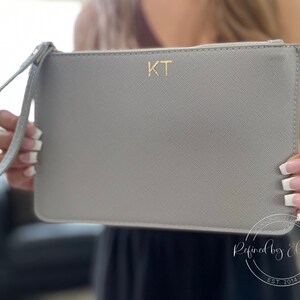 Person holding personalized grey clutch bag with gold initials.