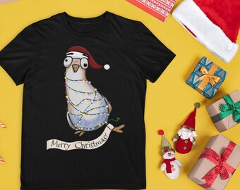 Könnte beinhalten: Schwarzes T-Shirt mit einer Cartoon-Taube, die einen Weihnachtsmannhut und eine Brille trägt und mit Lichterketten umwickelt ist. Das Shirt hat ein Banner mit der Aufschrift "Merry Christmas!" umgeben von Weihnachtsdekorationen.
