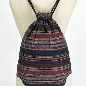Può includere: Uno zaino nero con coulisse e strisce multicolori in tonalità di rosso, rosa, giallo e bianco. Lo zaino ha coulisse nere ed è realizzato in tessuto intrecciato.