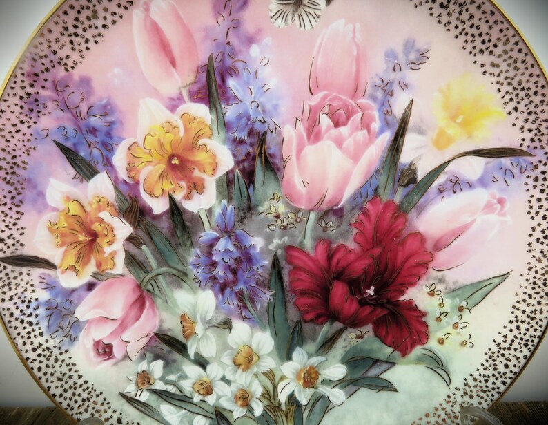 K&ouml;nnte beinhalten: Ein antiker Porzellan Teller mit einem Blumendesign mit rosa, gelben und roten Blumen. Die Blumen sind in einem realistischen Stil gemalt und von gr&uuml;nen Bl&auml;ttern umgeben. Der Teller hat einen goldenen Rand und einen wei&szlig;en Hintergrund.