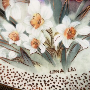 K&ouml;nnte beinhalten: Ein wei&szlig;er Porzellanteller mit einem Blumendesign mit wei&szlig;en Narzissen und gr&uuml;nen Bl&auml;ttern. Der Teller hat einen goldenen Rand und die Signatur "Lena Lih" ist unten rechts sichtbar.