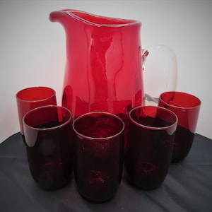 May include: A set of six red glass tumblers and a matching red glass pitcher. The pitcher has a clear glass handle.