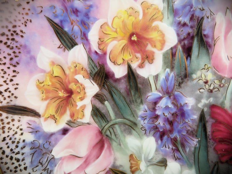 K&ouml;nnte beinhalten: Ein antiker Keramikteller mit einem Blumendesign mit rosa, gelben und blauen Blumen. Die Blumen sind realistisch gemalt und haben komplizierte Details. Der Teller hat einen wei&szlig;en Hintergrund mit einem dezenten Rosaton.