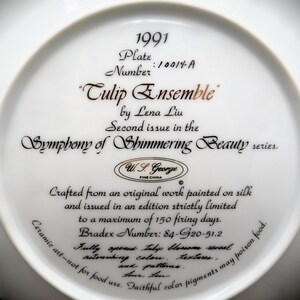 K&ouml;nnte beinhalten: Ein wei&szlig;er Keramikteller mit goldener Inschrift. Die Inschrift lautet "1991 Teller Nummer: 10014-A "Tulpenensemble" von Lena Liu Zweite Ausgabe in der Serie Symphonie der schimmernden Sch&ouml;nheit. W.S. George FEINE PORZELLAN Hergestellt aus einem Originalwerk, das auf Seide gemalt wurde, und in einer streng limitierten Auflage von maximal 150 Brenntagen herausgegeben. Bradex-Nummer: 84-G20-51.2 Die vollst&auml;ndig ge&ouml;ffnete Tulpenbl&uuml;te enth&uuml;llt erstaunliche Farben, Texturen und Muster. Keramikkunst - nicht f&uuml;r den Verzehr geeignet. Treue Farbpigmente k&ouml;nnen Lebensmittel vergiften."