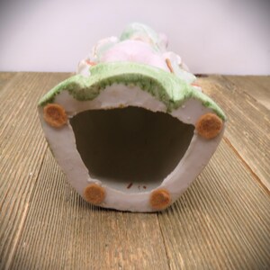 May include: The bottom of a porcelain figurine with a green, pink, and white design. The figurine has four felt pads on the bottom.