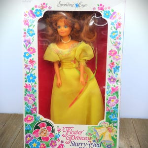 May include: A vintage doll in its original box. The doll is wearing a yellow dress and a pearl necklace. The box is decorated with floral designs and the text "Sparkling Eyes", "Flower Princess Starry-eyed Bride". The doll is 29.2 cm tall.