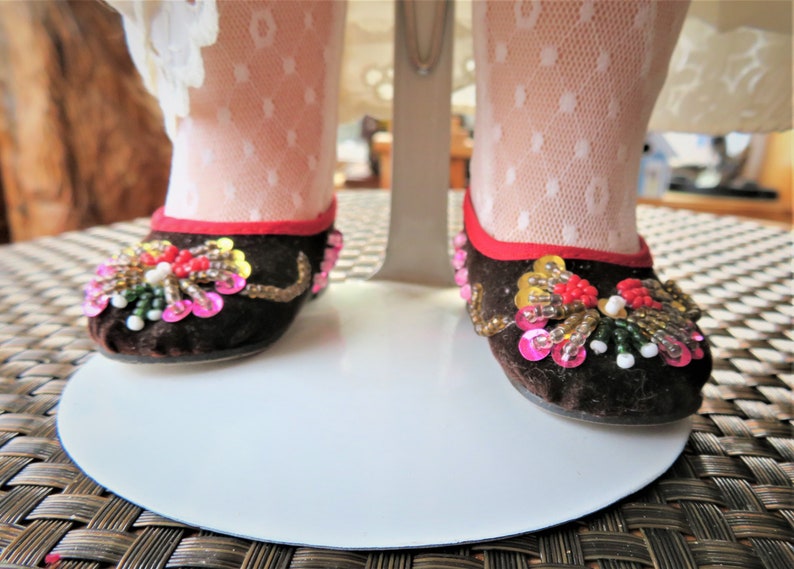 May include: A pair of brown velvet shoes with red trim and colorful beaded embellishments.