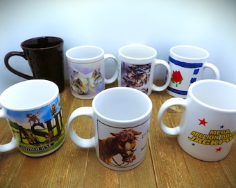 May include: Seven ceramic coffee mugs with various designs. The mugs feature images of animals, landscapes, and text. The mugs are all white except for one brown mug.