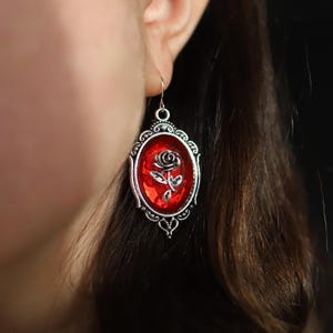 Może przedstawiać: Srebrne kolczyki z czerwonym szklanym kameą przedstawiającym czarną różę.