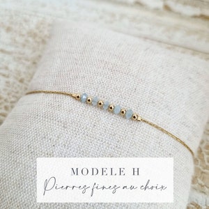 Puede incluir: Un delicado brazalete de cadena dorada con una fila de cuentas de piedras finas de color azul claro. El brazalete tiene un cierre deslizante y está etiquetado "MODELE H Pierres fines au choix".