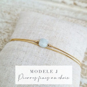 May include: A delicate gold chain bracelet with a light blue gemstone. The bracelet is adjustable and features a sliding knot closure. The text "MODELE J Pierres fines au choix" is visible in the image.
