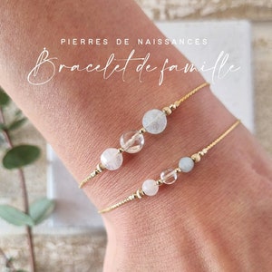 Può includere: Due delicati braccialetti a catena dorata con perline di pietre preziose. Il braccialetto superiore ha tre perline: un quarzo trasparente, una pietra di luna bianca e una pietra di luna bianca nuvolosa. Il braccialetto inferiore ha tre perline: un quarzo trasparente, un acquamarina blu chiaro e un quarzo rosa rosa. I braccialetti sono etichettati "Bracelet de famille" e "Pierres de Naissances".