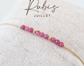 Op de afbeelding: Een delicate gouden kettingarmband met een rij kleine, gefacetteerde roze robijnkralen, afgewisseld met twee piepkleine, getextureerde gouden tussenkralen. De tekst Rubis JUILLET staat in bruine letters boven het sieraad afgebeeld.