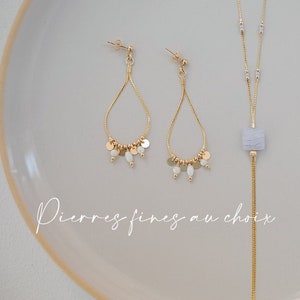 Könnte beinhalten: Ein Paar goldene Kettenohrringe mit weißen Perlen und kleinen goldenen Scheiben sowie eine goldene Kettenkette mit einem hellblauen Steinanhänger. Der Text "Pierres fines au choix" ist im Bild sichtbar.