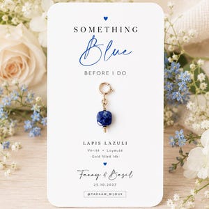 Op de afbeelding: Een 14k gold-filled bedel met een vierkante lapis lazuli kraal op een witte kaart. De kaart bevat de tekst SOMETHING Blue BEFORE I DO, LAPIS LAZULI, Vérité Loyauté, Gold filled 14k, Fanny & Basil, 25.10.2027 en @TADAAM_BIJOUX met blauwe hartjes.