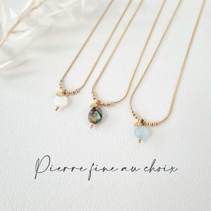 Peut inclure: Trois colliers en or avec des pendentifs en pierres précieuses différentes. Les colliers sont sur un fond blanc. Les pendentifs sont une pierre blanche, une pierre verte et noire, et une pierre bleu clair. Le texte "Pierre fine au choix" est écrit sous les colliers.