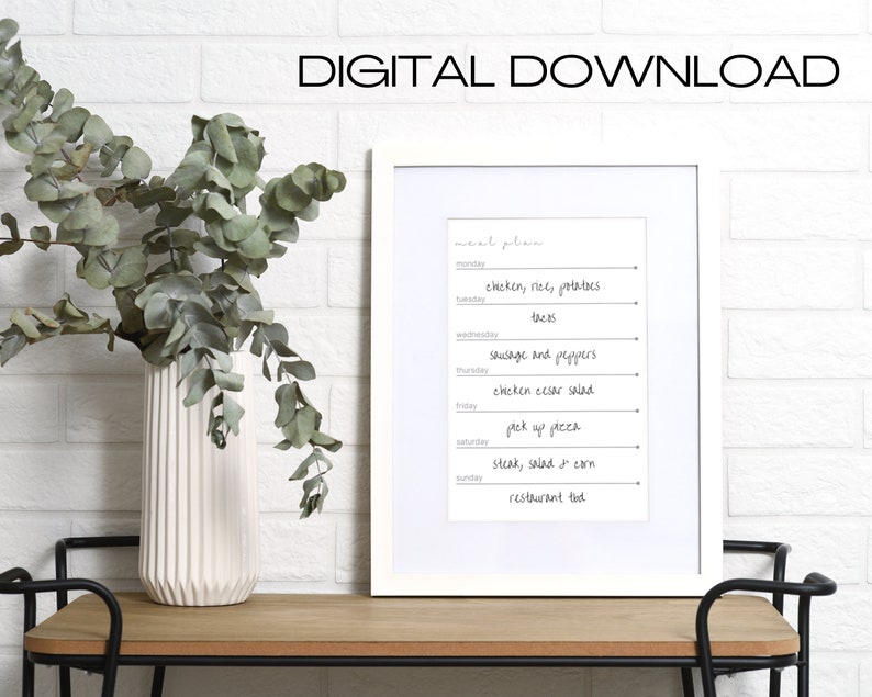 May include: A printable meal planner in a white frame on a wooden table. The planner includes a list of meals for each day of the week, such as "chicken, rice, potatoes" and "steak, salad & corn".