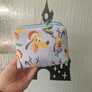 May include: A blue zippered pouch with a Christmas-themed print featuring Pluto and Goofy dressed as reindeer. The print includes holly, snowflakes, and a light blue background.
