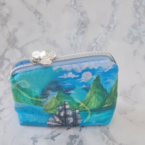 May include: A blue and green zippered pouch with a silver Mickey Mouse head zipper pull. The pouch features a printed image of a ship sailing past a tropical island.