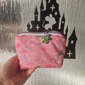May include: Pink zippered pouch with a rainbow, cloud, and donkey print. The pouch has a zipper pull with a rose charm. The text on the pouch reads "cause I know what my worth is".