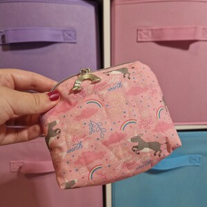 May include: Pink fabric coin purse with a rainbow clasp. The purse features a pattern of unicorns, rainbows, clouds, and the text "I know what my worth is." The purse has a silver zipper.