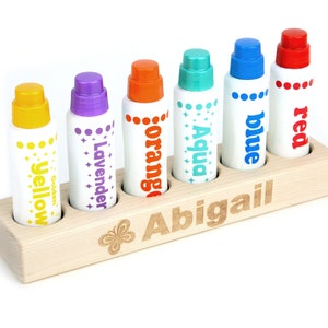 May include: Wooden organizer with six slots for markers. The slots are labeled with the colors of the markers: yellow, lavender, orange, aqua, blue, and red. The organizer is personalized with the name "Abigail" and a butterfly design.