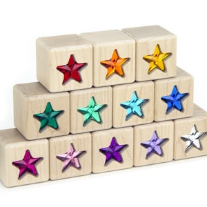 May include: A set of wooden blocks with colorful star-shaped inserts. The blocks are arranged in a pyramid shape, with the top block having a red star, the next row having orange, yellow, and blue stars, and the bottom row having green, turquoise, purple, light blue, and white stars.