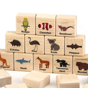 May include: Wooden alphabet blocks featuring colorful illustrations of Australian animals, including a budgie, clownfish, bandicoot, echidna, emu, koala, platypus, kangaroo, shark, dingo, Tasmanian devil, and wombat. Each block has the animal's name.